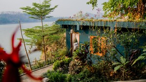 Uma casa isolada com vista para um lago, rodeada por vegetação exuberante e um caminho de pedra que leva à entrada.