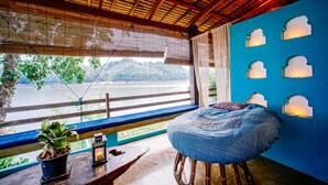 Quarto com vista para um rio, parede azul com luminárias de parede, um banco e um vaso com planta.