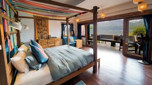 Um quarto espaçoso com uma cama grande, cabeceira de madeira e vista para um lago através de amplas janelas.