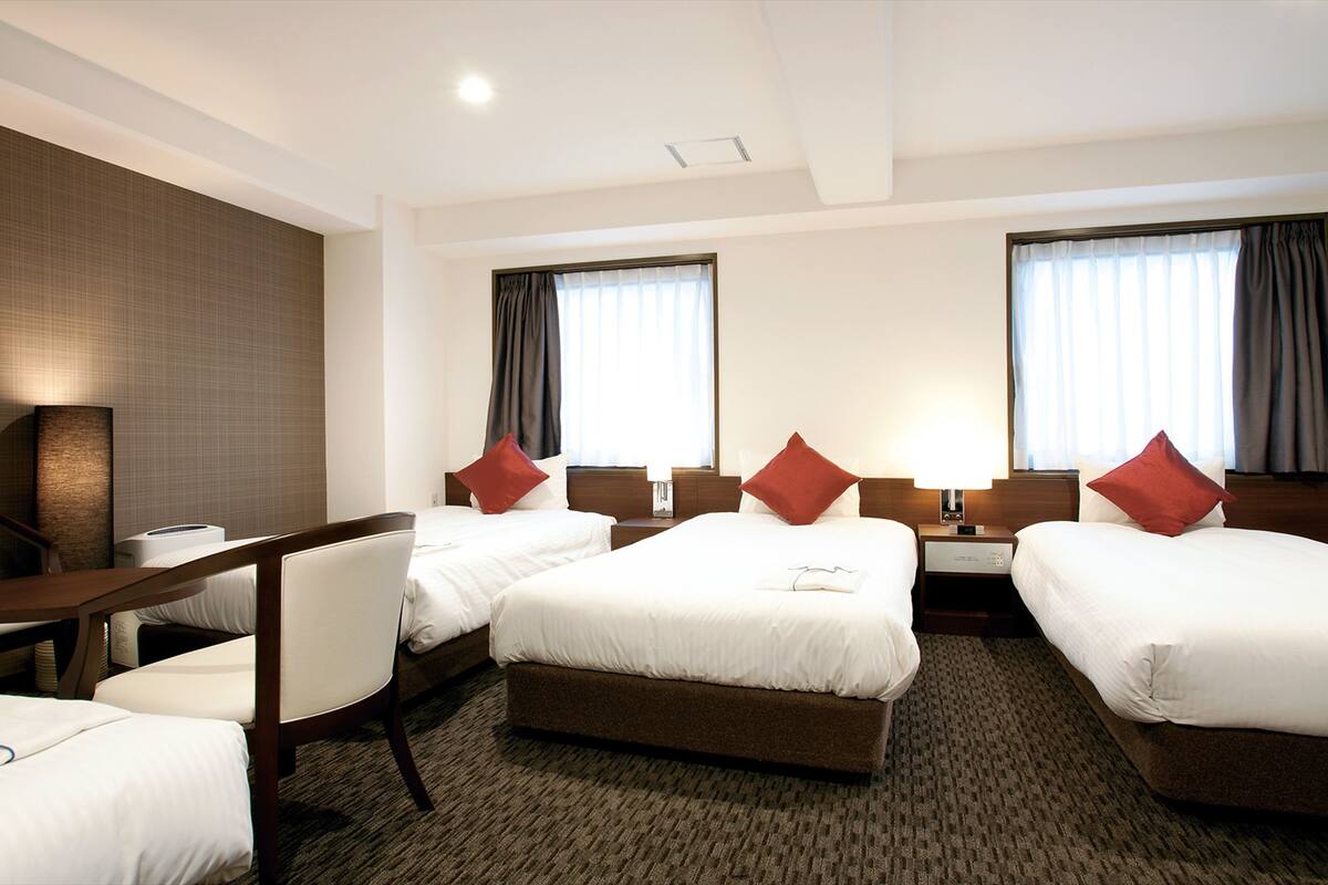 A hotel room with two single beds, a desk, and a chair.