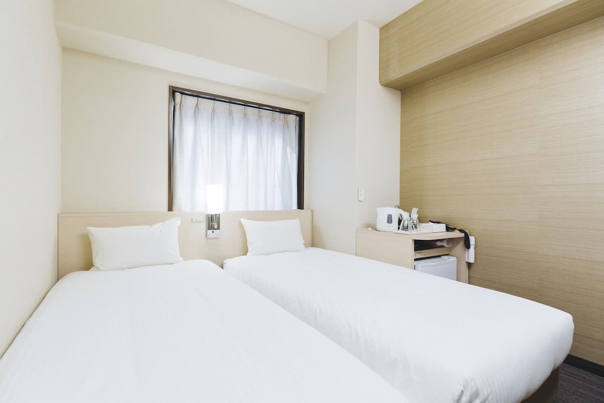 A hotel room with two single beds, a bedside table with a lamp, a coffee maker, and a telephone.