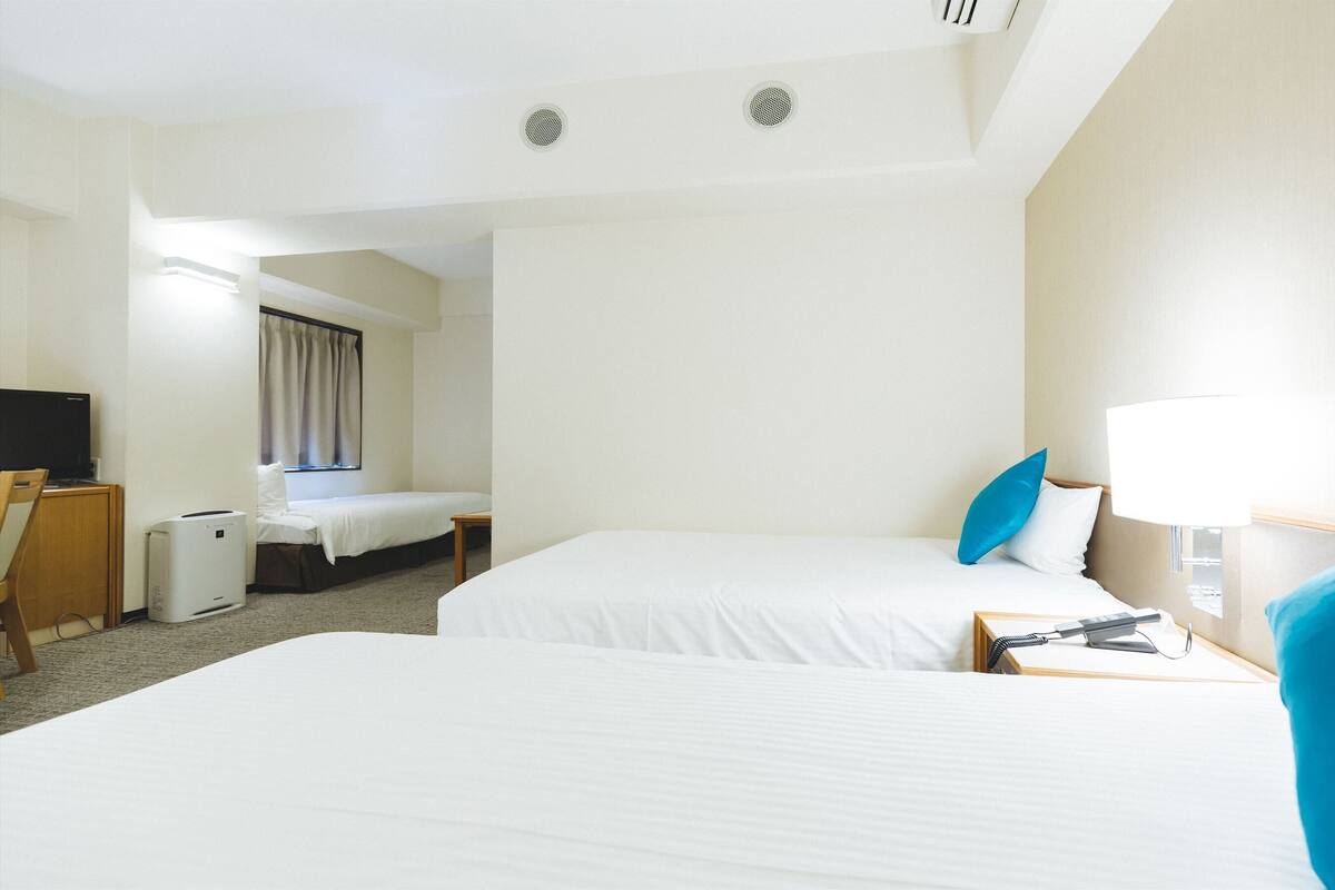A hotel room with two beds, a desk, a chair, a TV, and a window with curtains.