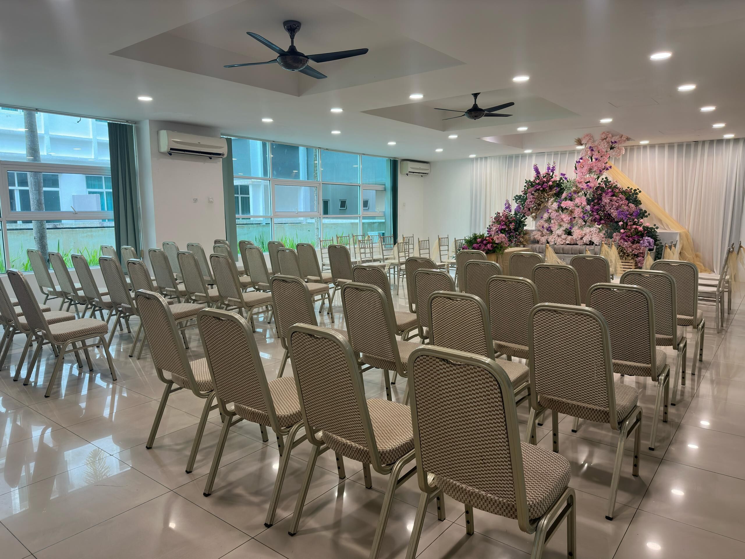 A conference room with rows of chairs, ceiling fans, and large windows.