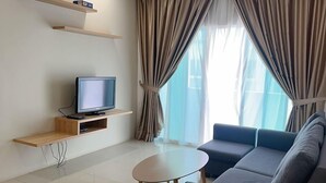 A modern living room with a flat-screen TV on a wooden shelf, a ceiling fan, a sofa, a small round table, and large windows with curtains. - D'Embassy Serviced Residence Suites (Kuantan)
