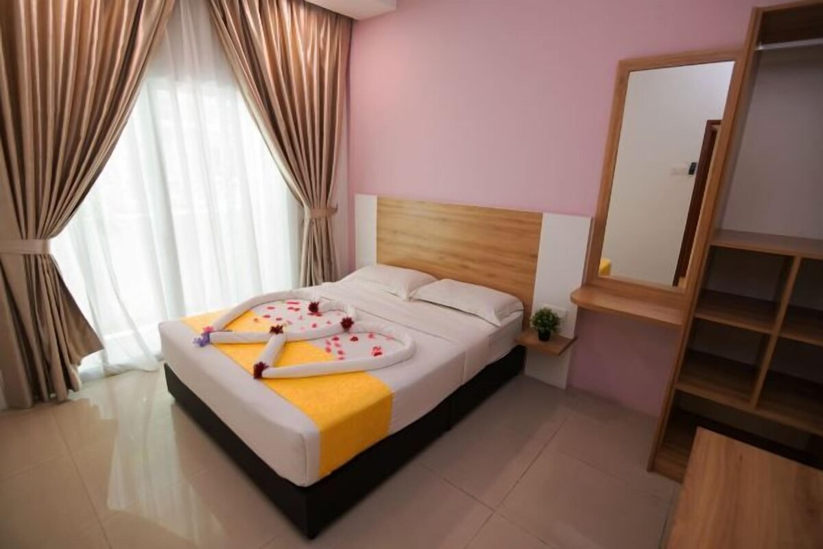 Una cama bien hecha con una toalla y pétalos de rosa, una mesita de noche con una planta y un espejo en la pared.