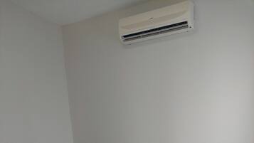 Un lit bien fait, avec du linge de lit blanc et une serviette pliée, une tête de lit en bois et un appareil de climatisation fixé au mur.