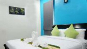 A neatly made bed with white linens and green pillows, a small framed picture on the wall, and a blue accent wall. - Lanta Memory Resort (Ko Lanta)