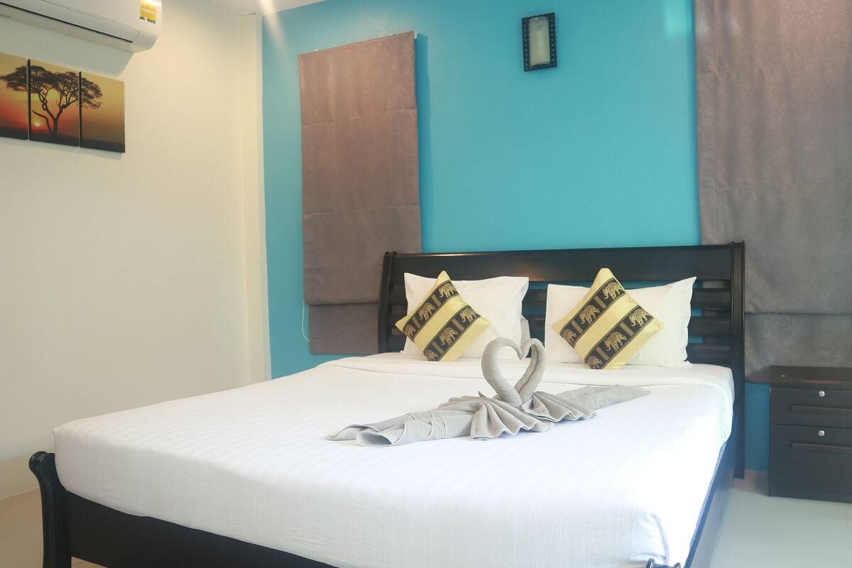 A neatly made bed with white linens, two decorative pillows with animal prints, and a towel arranged in a heart shape.