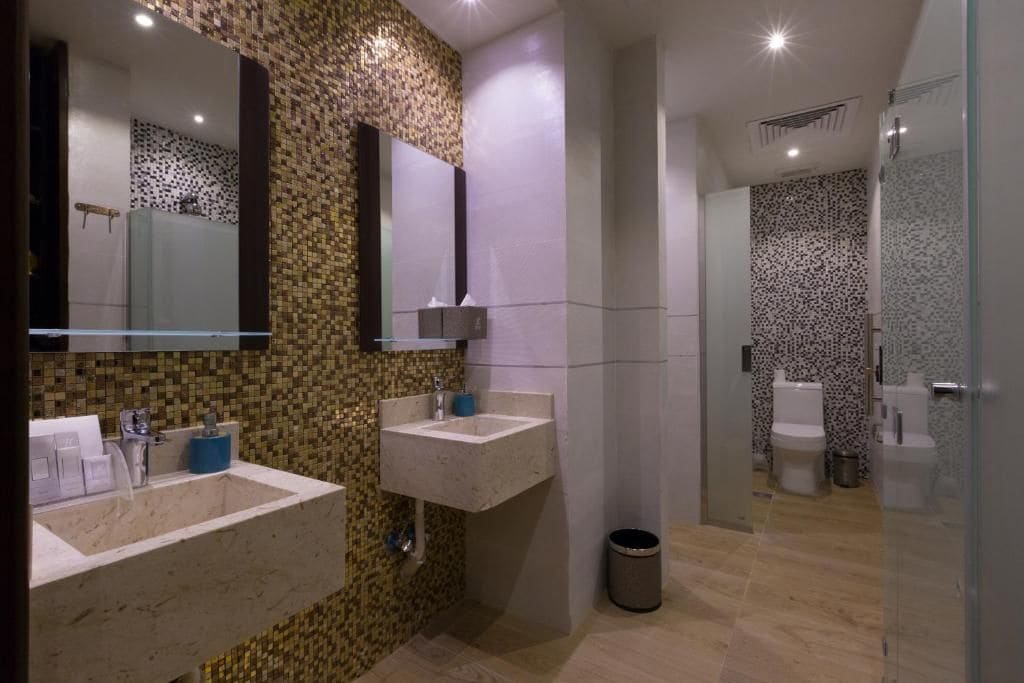 A modern bathroom with two sinks, a mirror, a shower area, and a trash bin.
