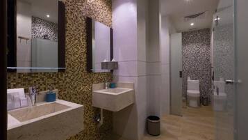 A modern bathroom with two sinks, a mirror, a shower area, and a trash bin.