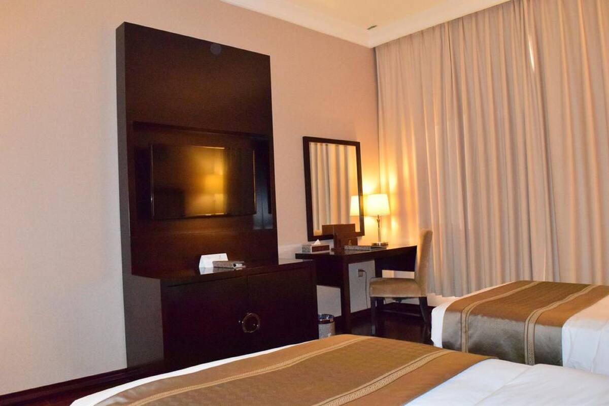 A hotel room with two beds, a TV, a desk, a chair, and a large window with curtains.