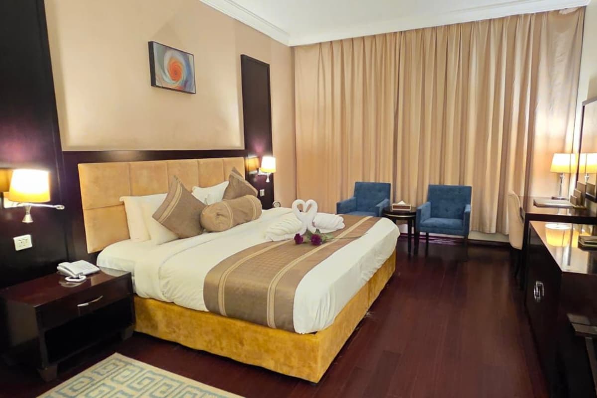 A hotel room with a large bed, two armchairs, a TV, and a desk.
