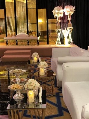 A luxurious hotel room with a plush sofa, a dining table with a floral centerpiece, and a decorative wall with vertical light fixtures.