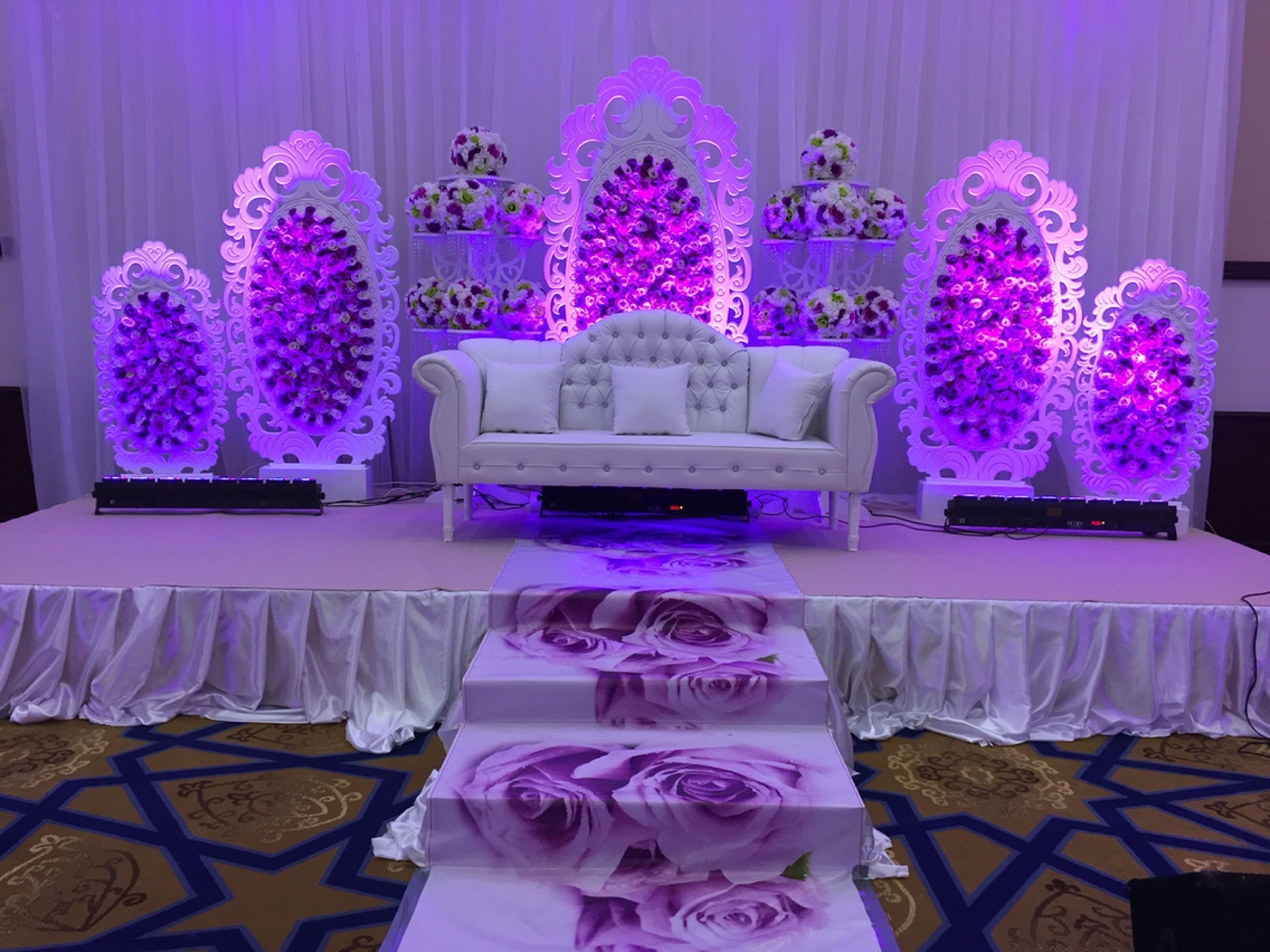 A stage with a white sofa, floral arrangements, and decorative lighting.