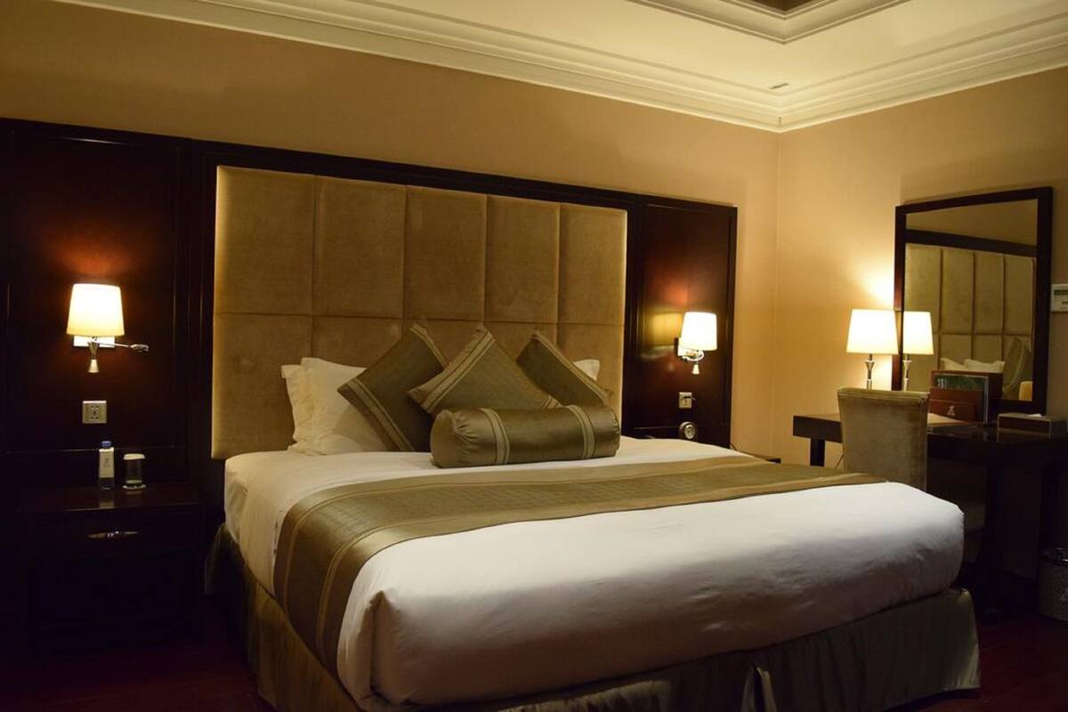 A hotel room with a large bed, two bedside lamps, a nightstand, a chair, and a mirror.