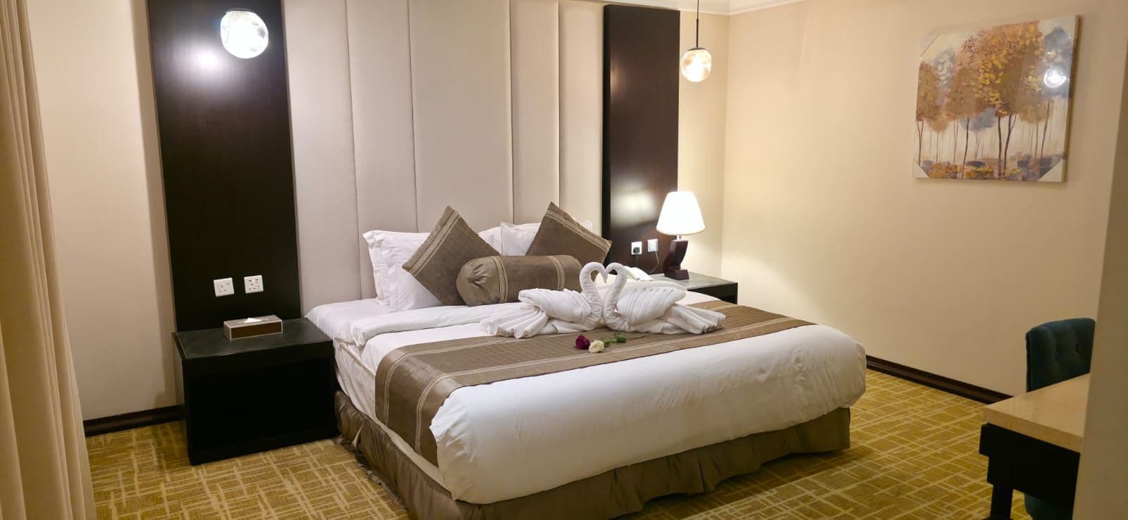 A hotel room with a bed, two bedside tables, a lamp, and a painting on the wall.