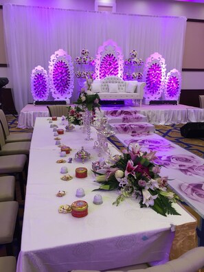 A banquet hall with a long table set for a formal event, featuring floral centerpieces and decorative items.