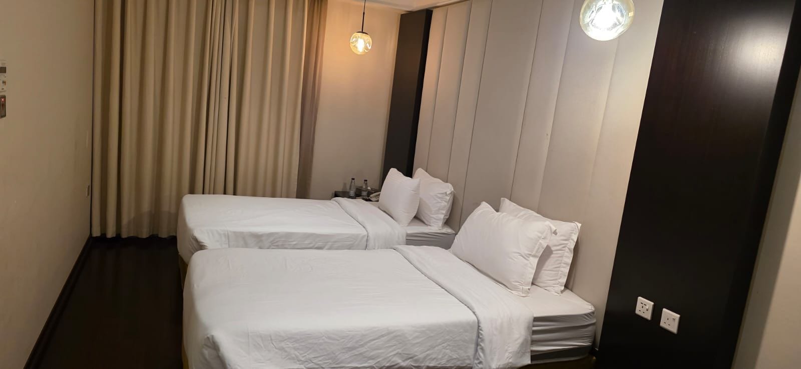 A hotel room with two beds, a curtain, a hanging light fixture, and a dark door.