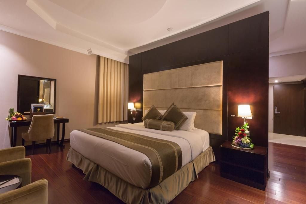 Habitación de hotel con una cama grande, un escritorio, una silla, una mesita de noche con lámpara y un espejo.