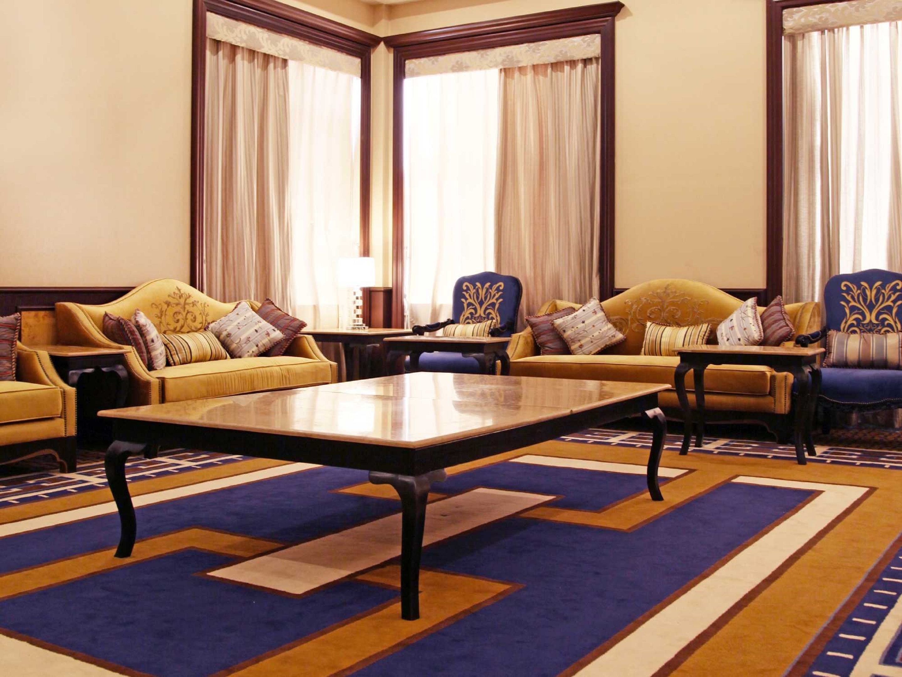 A spacious living room with a large central table, two sofas, and a patterned carpet.