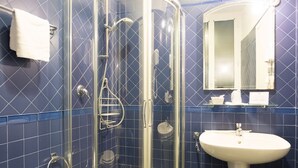 Un baño con cabina de ducha de vidrio, un lavamanos blanco y un espejo sobre el lavamanos.