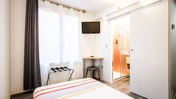 A hotel room with a bed, a TV mounted on the wall, a desk with a chair, and a sliding door leading to a bathroom.