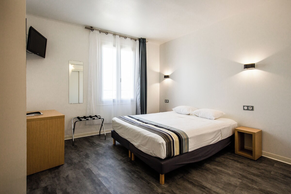 A modern bedroom with a bed, a desk, a TV, and two wall-mounted lights.