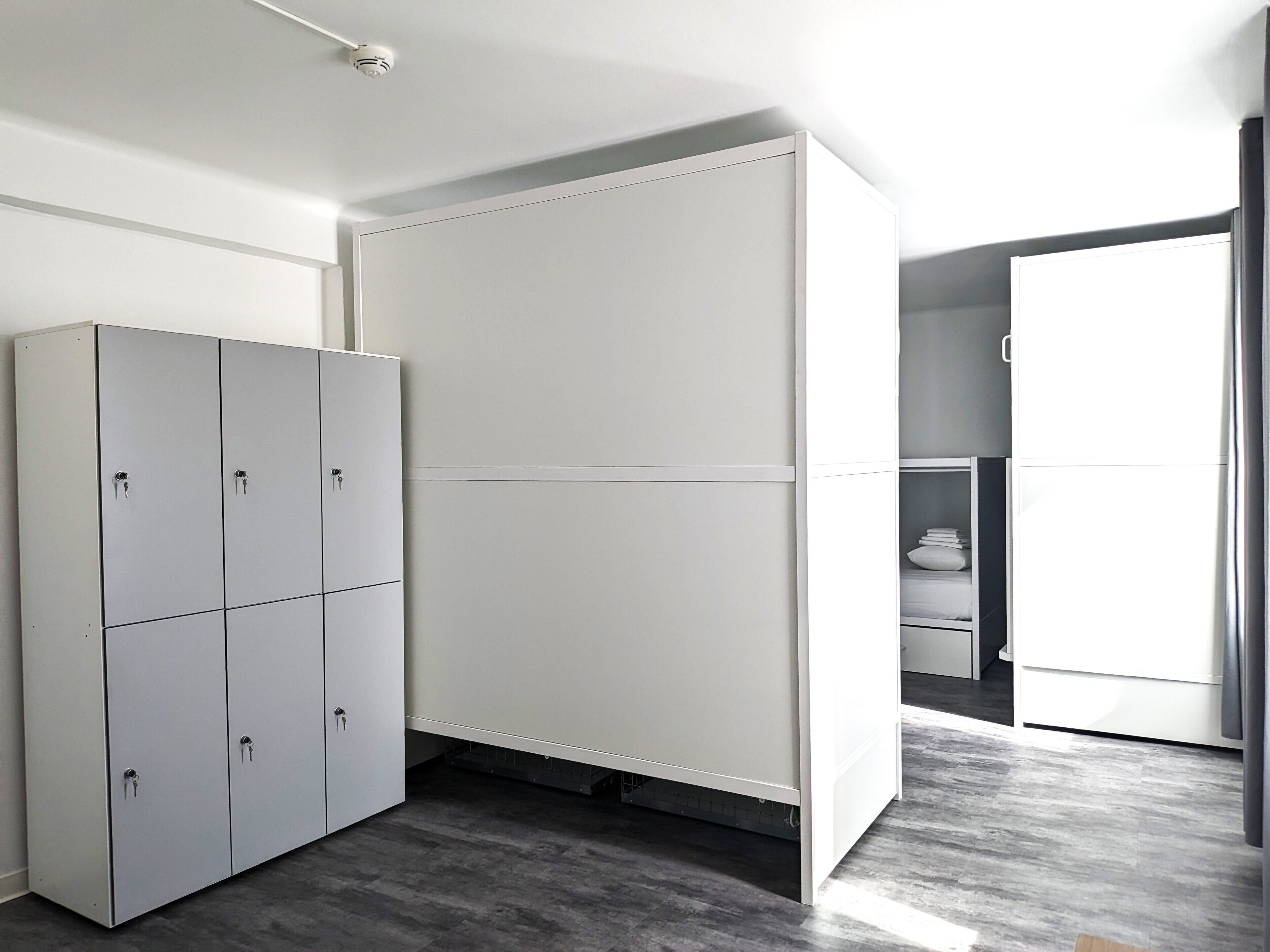 Una habitación moderna y minimalista con un armario gris, un mueble blanco y un baño a la vista.