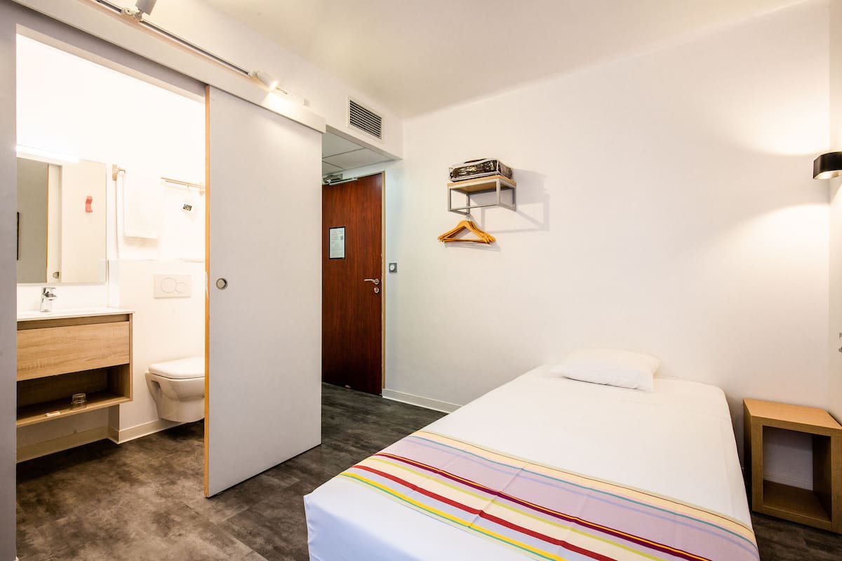 Habitación de hotel con cama, mesita de noche, armario, baño con inodoro y lavamanos, y espejo.