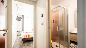 Una habitación de hotel con cama, ducha y televisión montada en la pared.