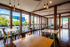 Un espace de restauration intérieur avec des tables et des chaises en bois, de grandes fenêtres et des luminaires suspendus.