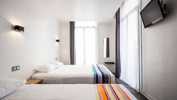 Habitación de hotel con dos camas, un televisor montado en la pared y una ventana con cortinas.