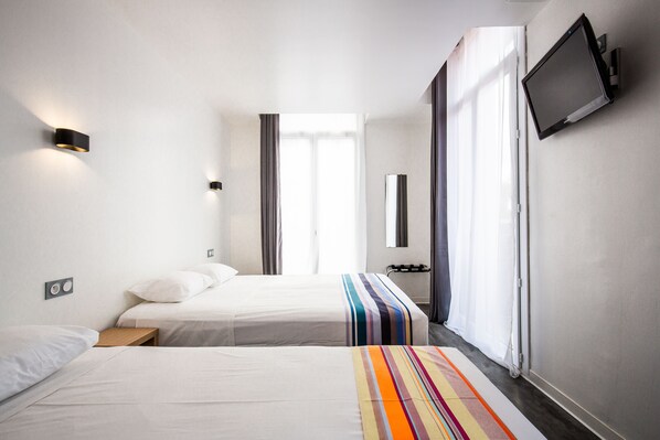 A hotel room with two beds, a TV mounted on the wall, and a window with curtains. - Hôtel PB - Paris-Barcelone (Perpignan)