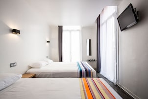 Habitación de hotel con dos camas, un televisor montado en la pared y una ventana con cortinas.
