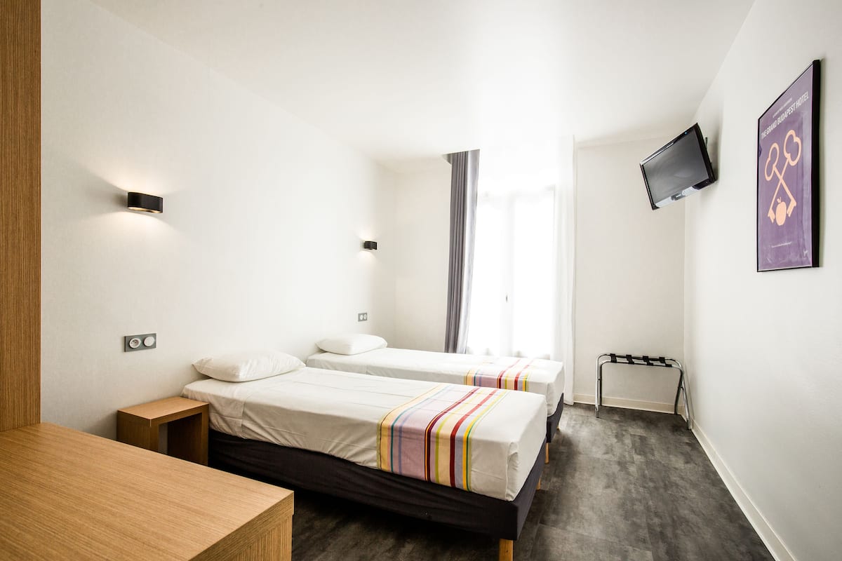 Habitación de hotel con dos camas, un escritorio, un televisor montado en la pared y una ventana con cortinas.