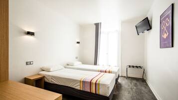 A hotel room with two beds, a desk, a TV mounted on the wall, and a window with curtains.