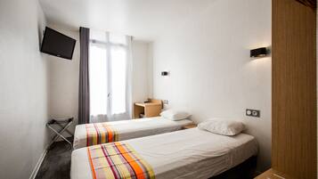 Une chambre d’hôtel avec deux lits, un téléviseur fixé au mur, une armoire en bois et un petit bureau avec une lampe.