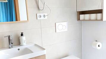 Un baño moderno con lavamanos blanco, tocador de madera, secador de pelo, inodoro y espejo.