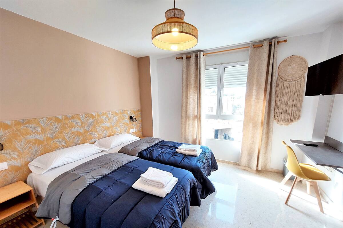 A hotel room with two beds, a desk, a chair, a television, and a window with curtains.