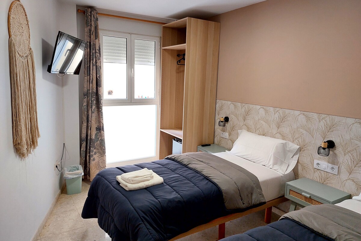A bedroom with a bed, a nightstand, a TV mounted on the wall, and a window with curtains.