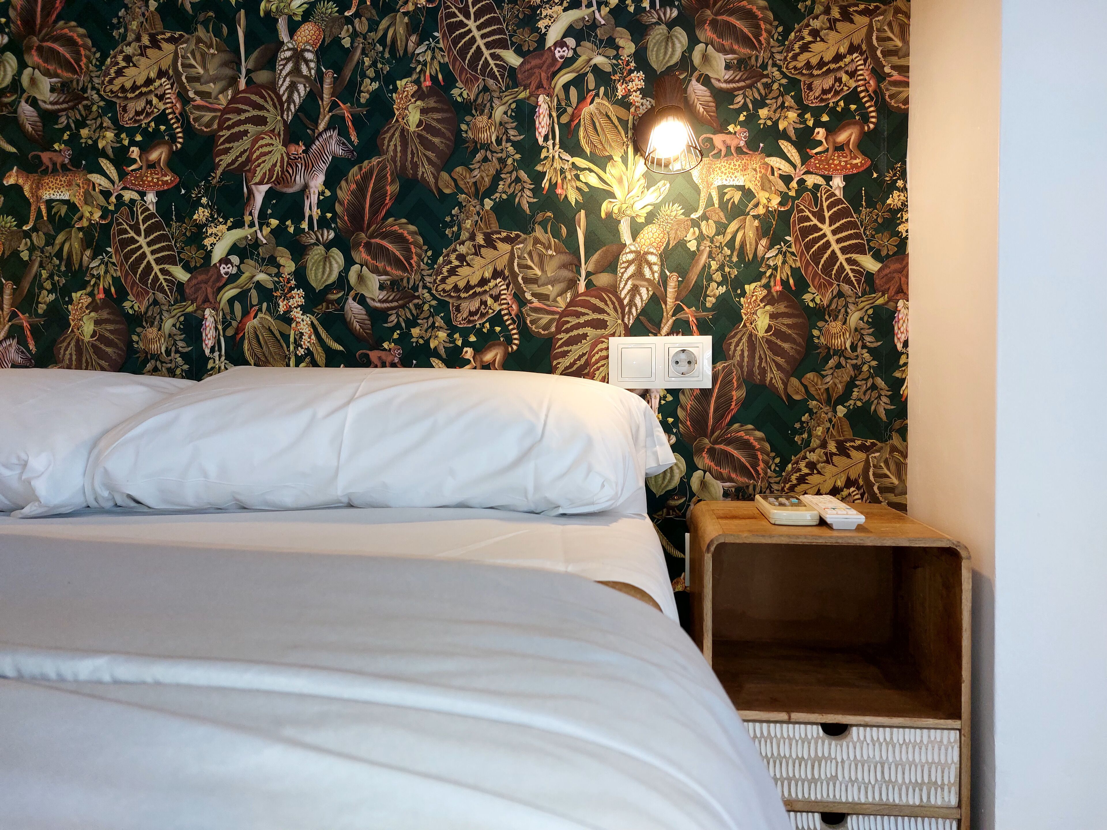 Un dormitorio con una cama, una mesita de noche y una pared con diseño floral.