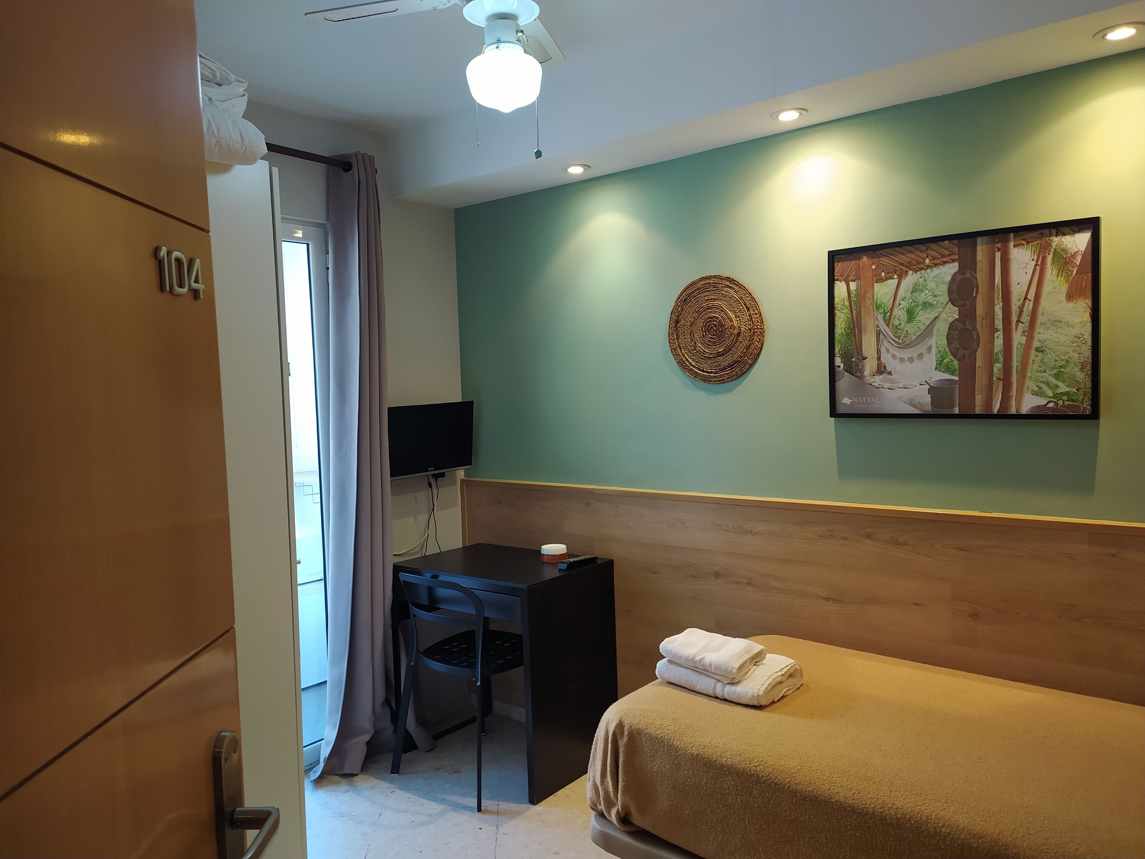 A hotel room with a bed, a desk, a chair, a television, and a wall-mounted artwork.