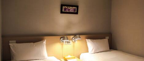 A hotel room with two single beds, a nightstand with a lamp, and a framed picture on the wall.