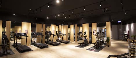 A gym with treadmills, elliptical machines, and stationary bikes arranged in rows.