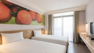 Camera d'albergo con due letti, un quadro di grandi dimensioni a tema frutta, una scrivania con televisore e una finestra con tende.