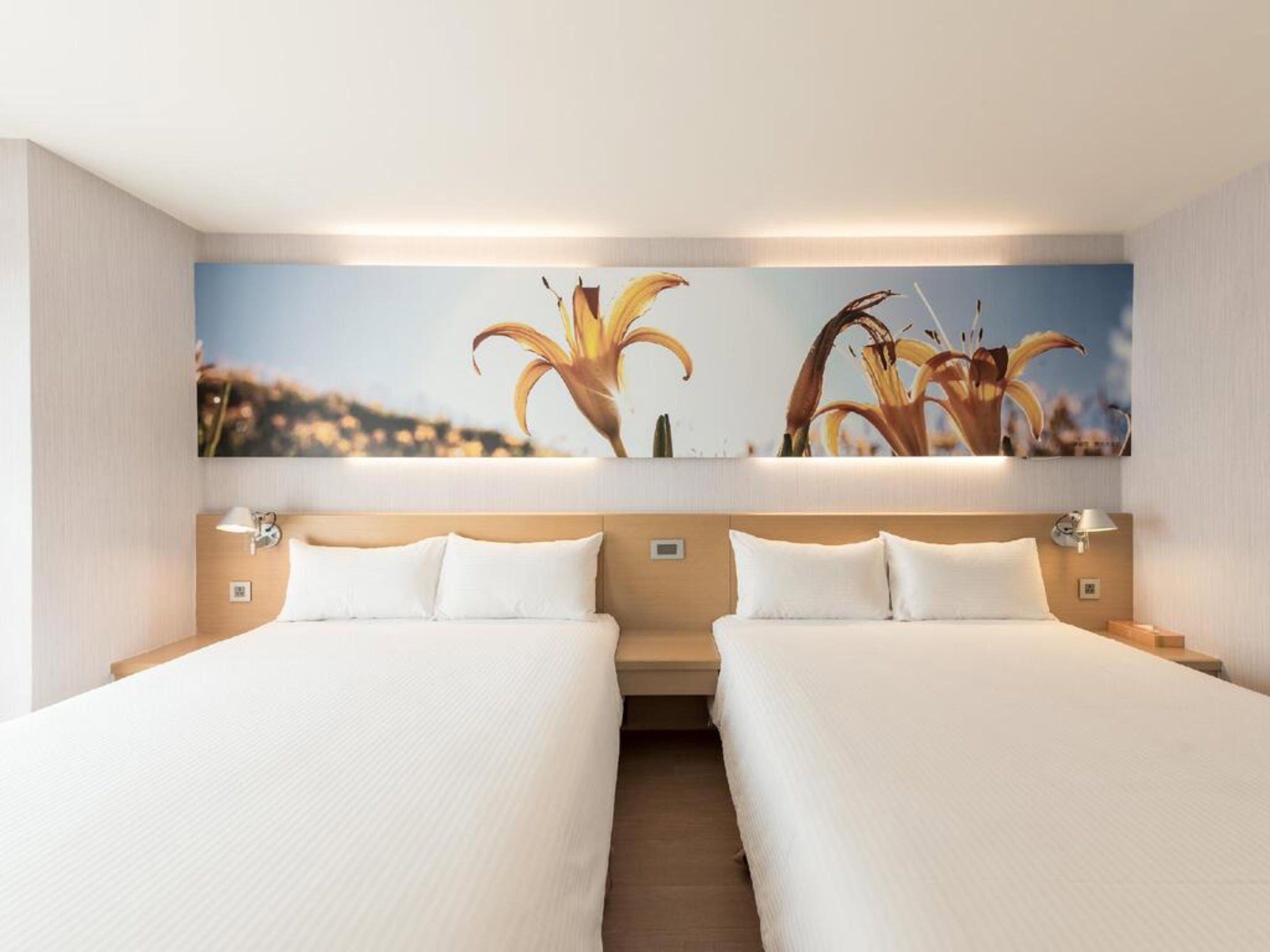 A hotel room with two single beds, a large wall-mounted artwork of flowers, and a neutral color scheme.