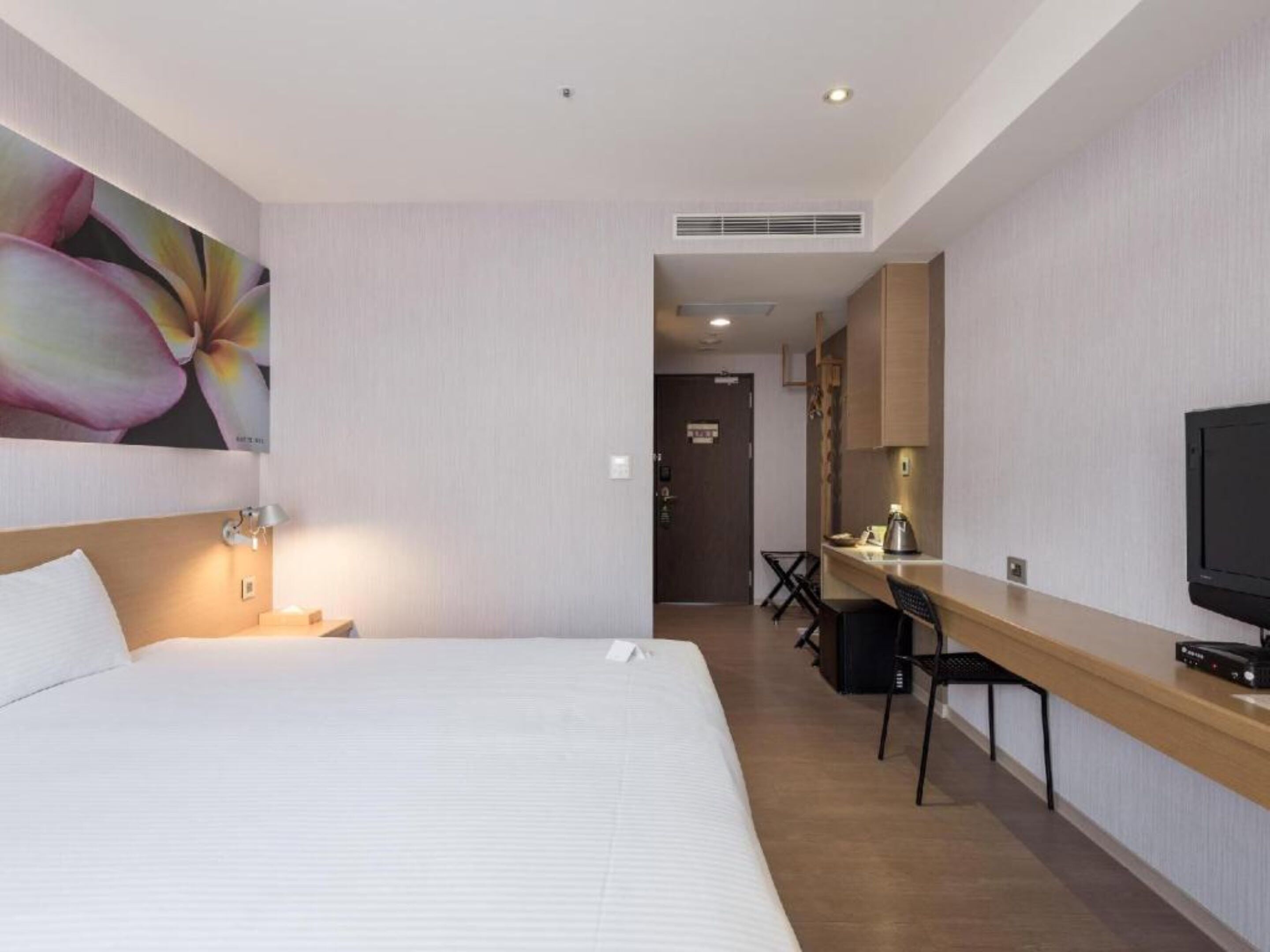 A hotel room with a bed, a desk with a TV, and a painting on the wall.