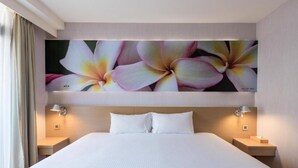 Habitación de hotel con una cama grande, dos mesitas de noche y una obra de arte floral colgada en la pared.