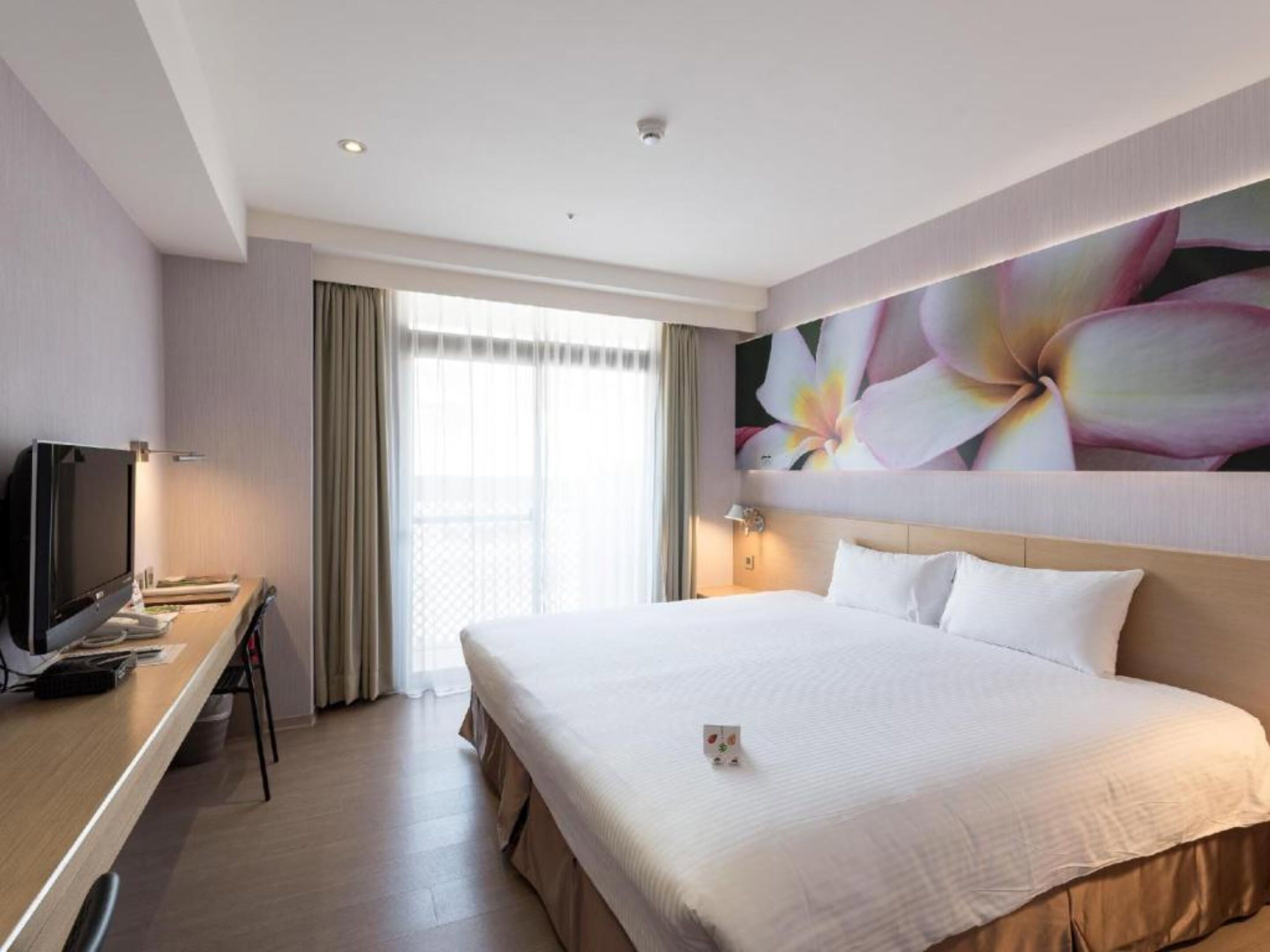 A hotel room with a large bed, a desk with a TV, and a window with curtains.