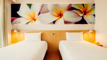 Une chambre d’hôtel avec deux lits, une grande œuvre d’art florale au-dessus des lits et des lampes de chevet.